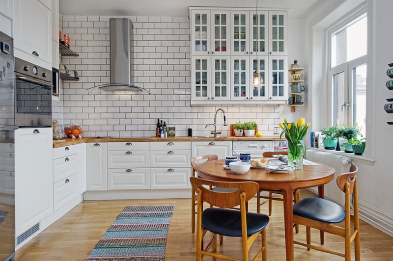 Красивый настенный шкафчик, качественный деревянный обеденный стол со стульями и кирпичная стена в интерьере скандинавской кухни