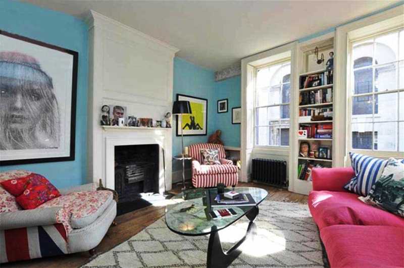 Незамысловатая гостиная с камином, стеклянным столиком, розовым диваном, голубыми стенами и белым потолком