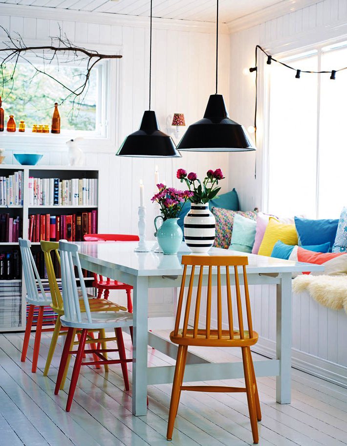 Дизайн столовой с разноцветными стульями и уютным уголком у окна с яркими подушками