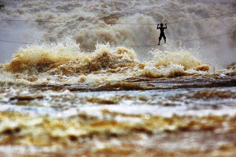 Лаосский рыбак перебирается по мосту, сделанному из натянутых проводов. Он пытается пересечь бурную реку Меконг в провинции Чампасак, Лаос